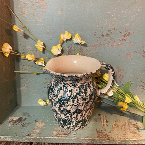 May include: A green and white speckled ceramic pitcher with a handle. The pitcher is sitting in a wooden box with a green painted interior.