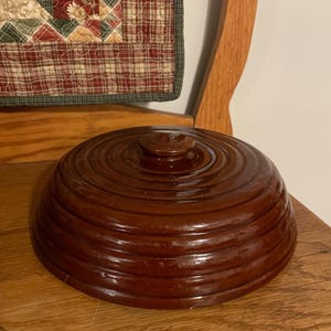 May include: A brown ceramic dome lid with a rounded top and a knob. The lid has a concentric circle pattern.