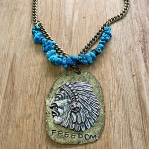 May include: A turquoise and brass necklace with a pendant featuring a silver profile of a Native American wearing a headdress. The pendant has the word "FREEDOM" inscribed on it.