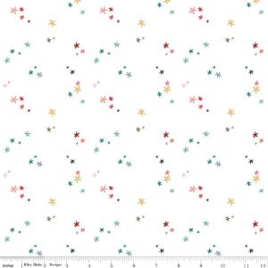 May include: A white fabric featuring a repeating pattern of small, multi-colored star-like shapes in shades of red, yellow, teal, and dark blue. A ruler at the bottom shows a scale of 12 inches, with the text Riley Blake Designs visible.