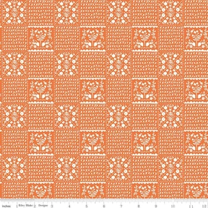 May include: Orange fabric with a repeating pattern of white floral and tree designs within a grid. The fabric has a textured appearance, with a ruler along the bottom edge showing inches.