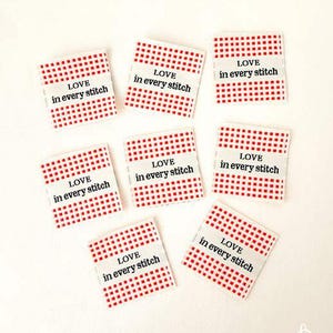 May include: Nine square fabric labels with a red and white checkered pattern. Each label has the text "LOVE in every stitch" printed in black on a white banner.