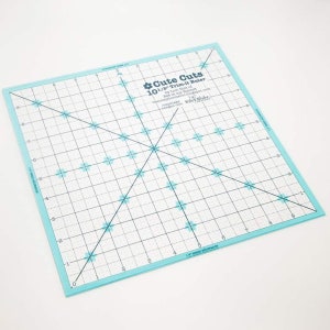 May include: A light blue 10 1/2 inch trim-it ruler with a grid pattern and a black diagonal line. The ruler has a floral design and the text "Cute Cuts" and "Trim-it Ruler" printed on it.