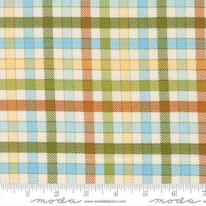 May include: A close-up of a fabric with a plaid pattern. The pattern features a grid of intersecting lines in shades of blue, green, orange, and yellow on a cream background. The fabric has a ruler along the bottom with the word "moda" and the website address.