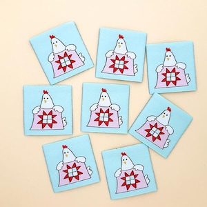 May include: Eight square patches with a light blue background, each featuring a white chicken with a red comb and a pink shawl. The chicken is holding a red and white star-shaped design. The patches are arranged in a circular pattern.