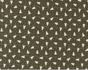 May include: A fabric with a repeating pattern of white Christmas trees and small white dots on a dark olive green background. The fabric has a ruler along the bottom edge with the word "moda" printed on it.