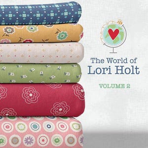 May include: A stack of colorful fabric rolls with floral and geometric patterns. The rolls are in shades of blue, yellow, white, green, red, and pink. The text "The World of Lori Holt VOLUME 2" is displayed on the right side of the image.
