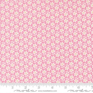 May include: Pink fabric with a repeating pattern of small white flowers with yellow centers and green stems. The fabric has a ruler along the bottom edge with the Moda Fabrics logo and website address.