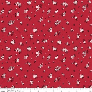 May include: A red fabric featuring a repeating pattern of small white flowers with black stems and leaves. A white ruler at the bottom edge shows a scale of 12 inches, indicating the print size and the text Riley Blake Designs.