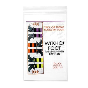 May include: A clear plastic package containing a Halloween-themed table runner pattern. The table runner design features black witch feet, orange, purple, and yellow blocks. Text on the package reads "Witches Feet Table Runner Pattern". The text "Trick or Treat Smell My Feet!" is also visible.