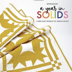 May include: A quilt booklet titled "a year in SOLIDS" by Riley Blake Designs and Jessica Dayon. The cover features a folded quilt with a yellow and white geometric pattern.