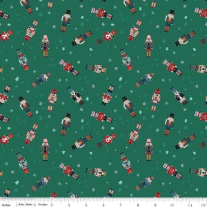 May include: A dark green fabric featuring a repeating pattern of nutcracker figures in various uniforms, interspersed with small white snowflakes and tiny light green pine trees. A white ruler is visible at the bottom, measuring 12 inches.