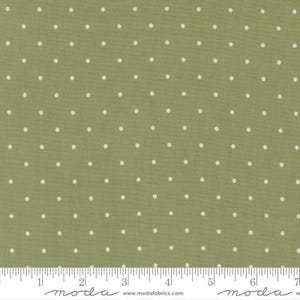 May include: A sage green cotton fabric featuring a repeating pattern of small, evenly spaced white polka dots. A white measuring tape is visible along the bottom edge, showing a scale of 7 inches across the width of the textile material.