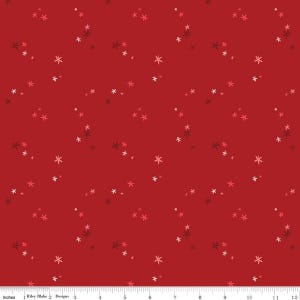 May include: A red fabric featuring a repeating pattern of small, scattered star-like shapes in shades of white, light pink, and dark red. A white ruler at the bottom indicates a scale of 12 inches, with the text Riley Blake Designs visible.