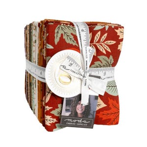 May include: A stack of folded fabric squares featuring a pattern of autumn leaves in shades of rust, cream, and sage green. The bundle is secured with a white ribbon printed with a ruler design, marked with 4 inches, and a Moda Fabrics tag.