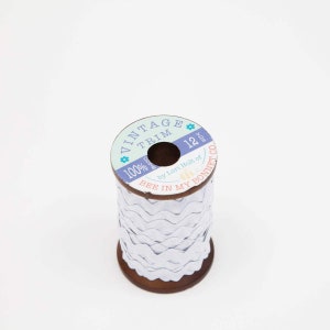 May include: A spool of white scalloped trim with a label that reads "Vintage Trim 100% Cotton 12 yds. by Lori Holt of Bee in My Bonnet Co."