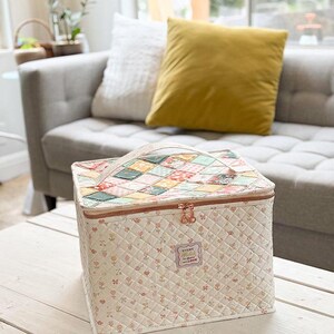 May include: A quilted cosmetic bag with a patchwork top and a floral pattern on the sides. The bag has a zipper closure and a handle. The text "Every stitch is done with love" is on the front.