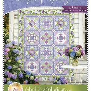 May include: A quilt with a floral design, featuring squares with star and diamond patterns in shades of purple, green, and white. The quilt is displayed outdoors with hydrangeas and the text "Bouquet of Hydrangeas" and "A 7-MONTH BLOCK OF THE MONTH".