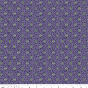 May include: A patterned fabric featuring a repeating design of green and gray rectangles, and small white dots on a dark purple background. The fabric is marked with inches along the bottom edge. The text "Riley Blake Designs" is visible.