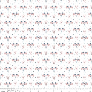 May include: White fabric with a repeating pattern of American flags, bows, and stars in red, white, and blue. The flags are clustered in groups of three. The fabric is marked with inches.