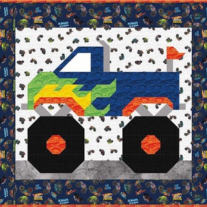 May include: A colorful quilt featuring a blue monster truck design. The truck has large black wheels and flame details in yellow, green, and orange. The background is white with small monster truck graphics, and the border is navy blue with more truck designs.