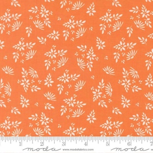 May include: A vibrant orange fabric featuring a repeating pattern of small white flowers and delicate leaves. A white measuring tape is visible at the bottom edge, showing a scale of 7 inches to provide a clear sense of the fabric's scale.