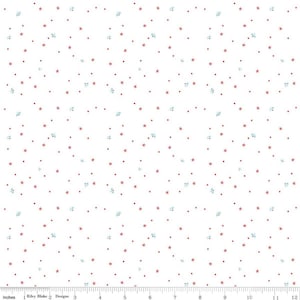 May include: White fabric with a repeating pattern of small red stars, tiny red dots, and clusters of light blue floral shapes. The fabric is marked with inches along the bottom edge. The text "Riley Blake Designs" is visible.