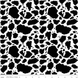 May include: A fabric featuring a repeating black and white cow print pattern. A white ruler with black markings is visible at the bottom, showing a scale of 12 inches. The text 'Riley Blake Designs' is printed on the ruler edge.