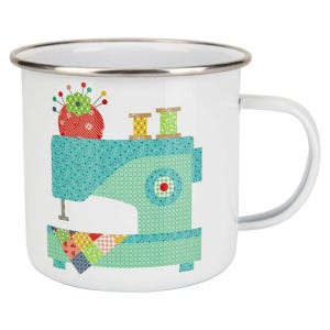 May include: White enamel mug with a silver rim and handle. The mug features a teal sewing machine design with a red pincushion, spools of thread, and a patchwork quilt detail. A charming gift for a seamstress.