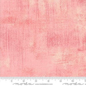 May include: A pink fabric with a textured, distressed look. The fabric has a subtle, faded pattern of horizontal and vertical lines. The fabric is shown with a ruler, with the text "moda" printed on the ruler.