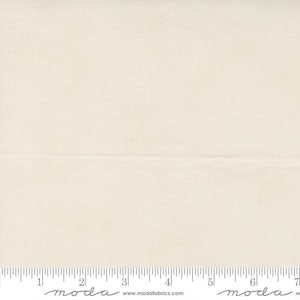 Puede incluir: Una tela de color blanco roto sólido con una textura tejida visible. Una regla blanca está colocada a lo largo del borde inferior, mostrando medidas en pulgadas de 0 a 7. El texto 'moda' y 'www.modafabrics.com' está impreso en la regla.
