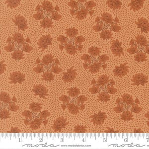 May include: A light orange fabric featuring a repeating pattern of dark orange floral clusters and a fine stippled dot texture. A white ruler at the bottom edge shows a scale of 7 inches, with the text moda and www.modafabrics.com printed.