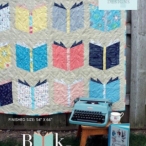 May include: A quilted blanket featuring a repeating pattern of open books in various colors. The quilt measures 54 inches by 66 inches. A vintage blue typewriter and a teacup are placed near the quilt. The text "Book Nerd" is displayed.