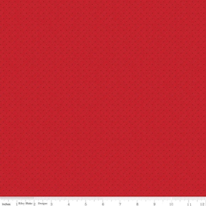 May include: Red fabric with a small, repeating dot pattern. The fabric is measured in inches, with a ruler along the bottom edge. The text "Riley Blake Designs" is visible.