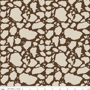 May include: A fabric pattern featuring an irregular, organic giraffe-like spot design in dark brown and light beige. A white ruler at the bottom edge shows measurements from 0 to 12 inches, indicating the scale of the repeating print.
