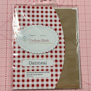 May include: A package of 14 count oatmeal colored evenweave fabric for cross stitch. The fabric is 19 by 21 inches and is 100% cotton. The package has a red and white gingham pattern.