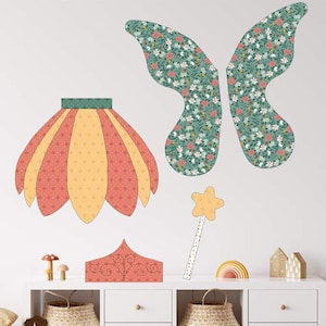 May include: A craft pattern titled "FAIRY DREAMS DRESS UP" featuring a fairy costume design. The design includes a skirt, wings, a wand, and a crown. The wings are green with a floral pattern. The skirt is orange and yellow. The pattern is child size.