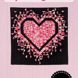 May include: A black and pink quilt with a heart design. The heart is filled with pink triangles and outlined in black. The quilt has the text "MINI Exploding Heart" at the top and a "Slice of Pi Quilts" logo at the bottom.