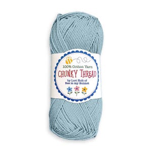 May include: A skein of light blue 100% cotton yarn with a white paper label. The label features a yellow bee icon, the text 100% Cotton Yarn, CHUNKY THREAD, by Lori Holt of Bee in my Bonnet, and three small colorful flower illustrations.