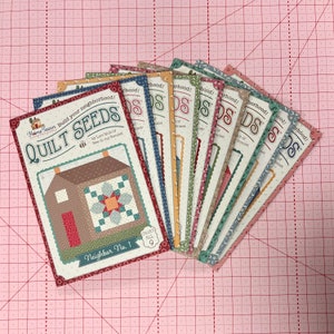 May include: A set of nine quilt patterns featuring a house with a patchwork quilt design. The patterns are titled "Quilt Seeds" and are part of a "Home Town" collection. The patterns are numbered 1 through 9 and are designed by Lori Holt of "Bee in my Bonnet".