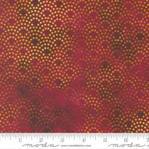 May include: A deep red fabric featuring a repeating pattern of gold metallic dots arranged in overlapping circular arcs. The textile has a mottled, textured appearance with darker shaded areas. A white ruler is visible at the bottom edge.