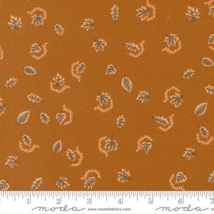 May include: A piece of fabric with a burnt orange background featuring a repeating pattern of small, dark brown leaves and curved vine-like sprigs. A white ruler at the bottom shows a scale of 7 inches for measuring the textile design.