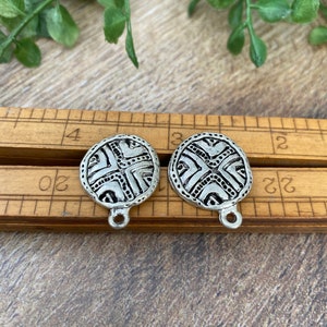 May include: Two silver-toned metal charms with a geometric design. The charms are oval-shaped and have a loop at the top for attaching to a necklace or bracelet.