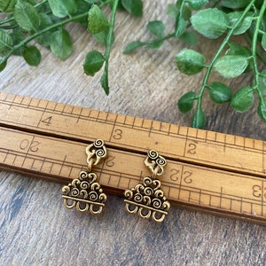 May include: A pair of gold-toned earrings with a swirling cloud design. The earrings are shown on a wooden surface with a ruler.