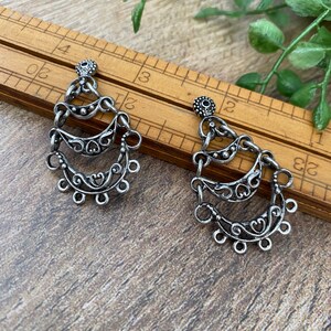 May include: A pair of silver dangle earrings with a delicate, intricate design. Each earring features three tiers of curved, openwork shapes with small beads and loops.