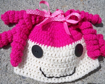 May include: A pink and white crocheted hat with a pink bow and black buttons. The hat has a smiling face.