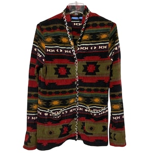 May include: A long-sleeved, button-down jacket with a Southwestern-inspired pattern. The jacket features a mix of red, black, green, and yellow geometric designs. White stitching accents the edges and pockets. The jacket is made of a soft, textured fabric.