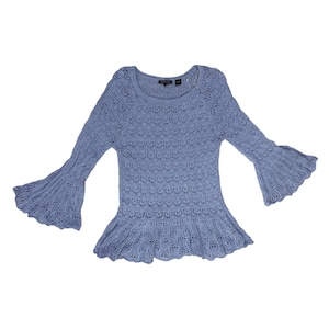May include: A light blue knit top with long, flared sleeves and a ruffled hem. The top has a round neckline and a delicate openwork pattern throughout the fabric. The sleeves are wide and bell-shaped, adding a dramatic flair to the design.