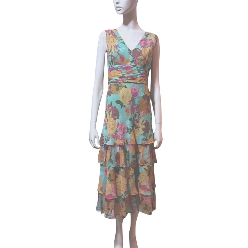 May include: A sleeveless, floral print dress with a V-neck and tiered skirt. The dress features a turquoise background with a pattern of yellow, pink, and orange flowers. The waist is cinched with a ruched band. The dress is displayed on a mannequin.