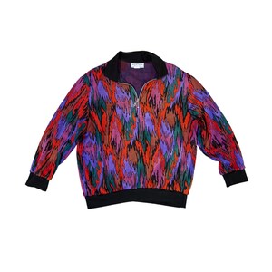 May include: A colorful zip-up sweatshirt with a vibrant pattern in shades of red, purple, green, and brown. The sweatshirt has a black collar, cuffs, and hem. The zipper is silver.